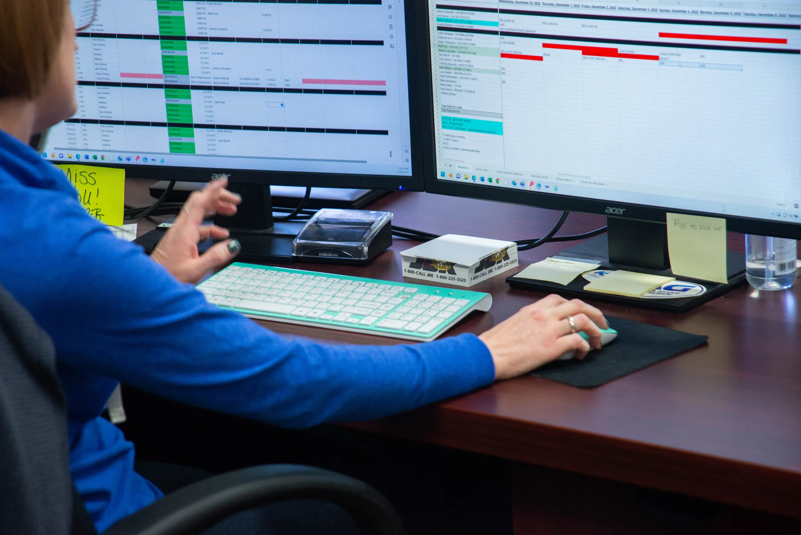 KAG dispatcher working at a desk with dual monitors showing a spreadsheet