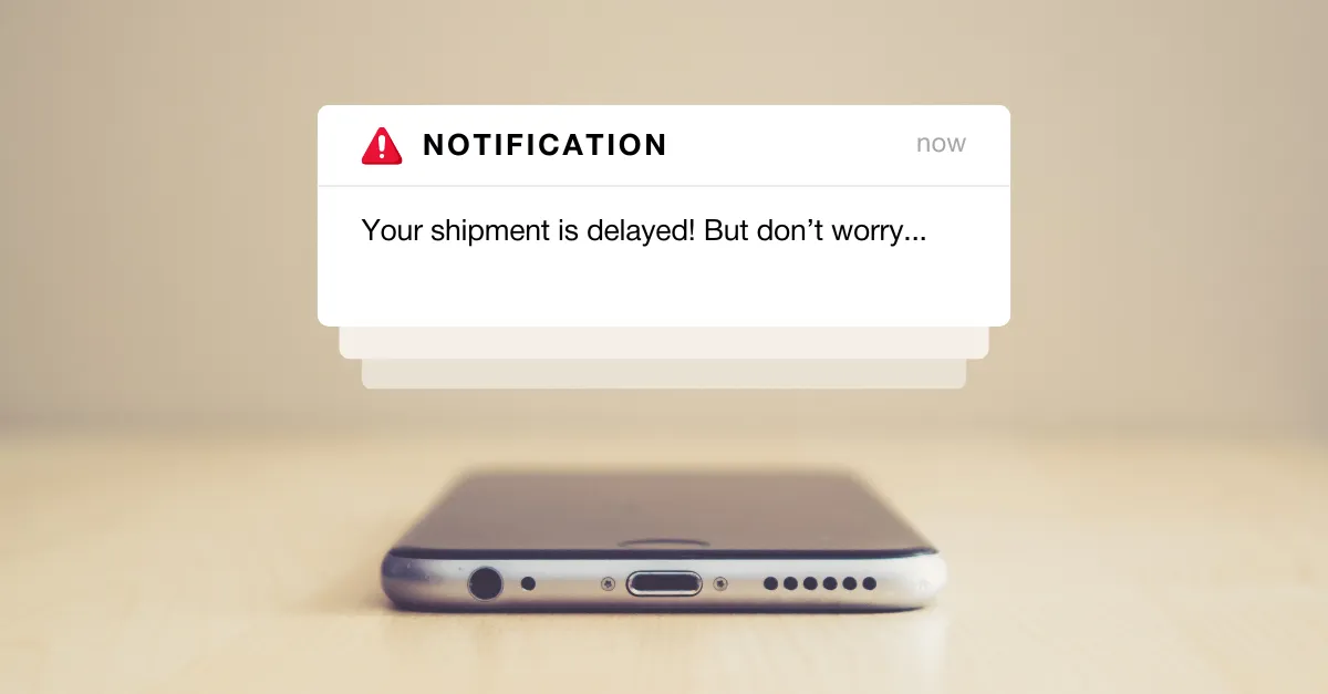 Phone on a desk with a notification reading "Your shipment is delayed! But don't worry…"
