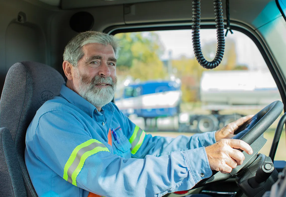 Smiling KAG driver in a jacket at the wheel of a truck cab