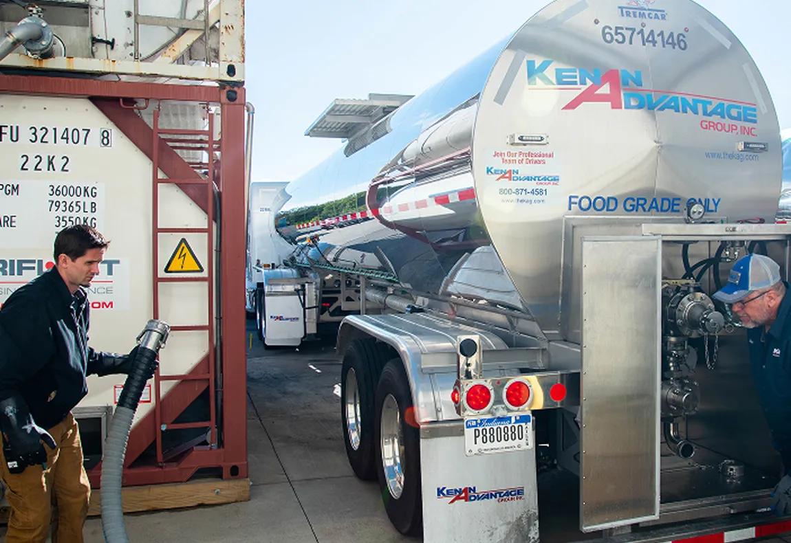 KAG worker connecting a hose to a Kenan Advantage food-grade tanker beside an container