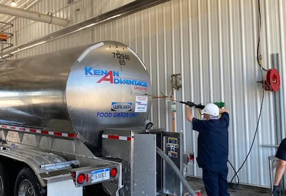 Worker cleaning a food-grade tanker trailer at a wash facility using high-pressure equipment to maintain transportation safety and sanitation standards.