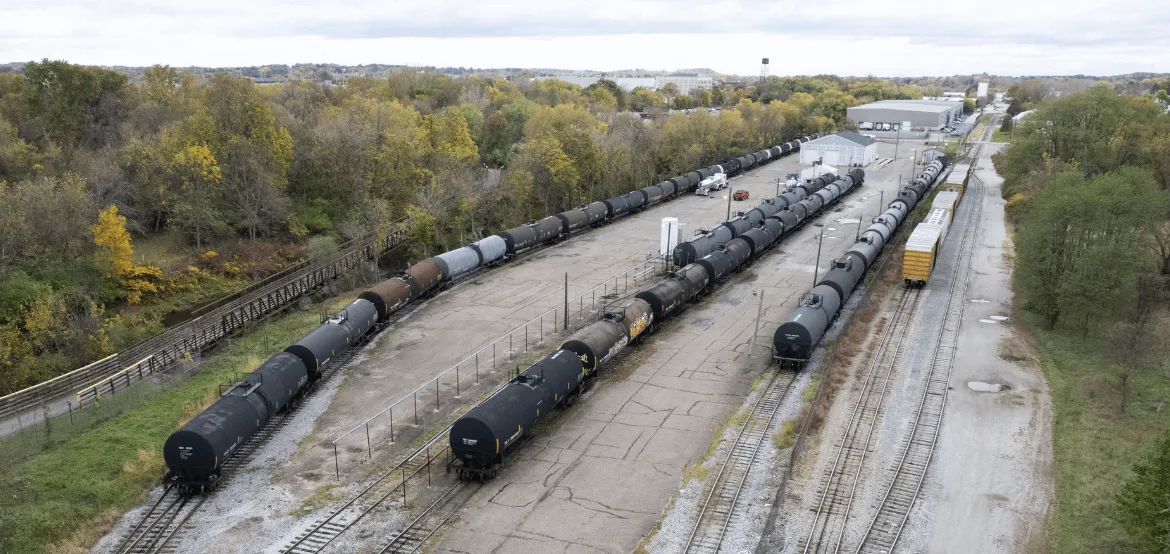 Aerial view of multiple rail tank car lines at a transloading facility surrounded by autumn trees