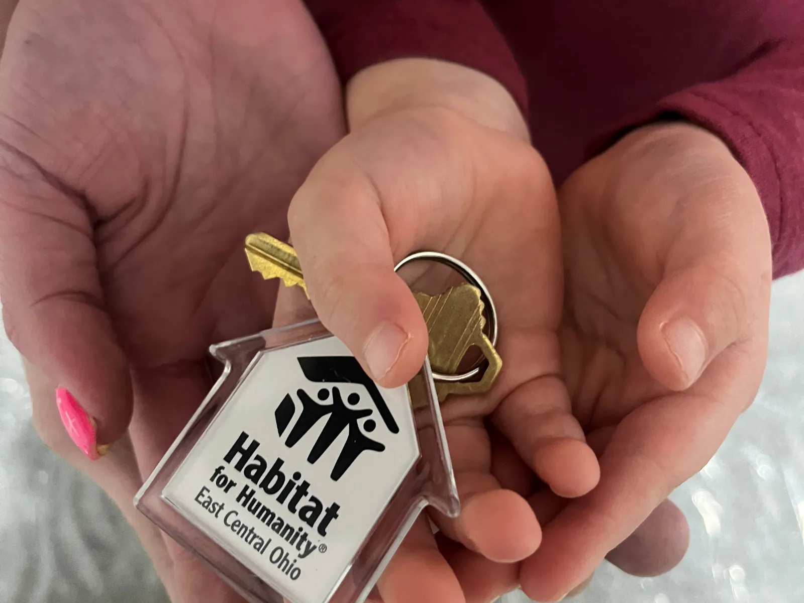 Child's hand holding a Habitat for Humanity East Central Ohio house key being passed from an adult's hand