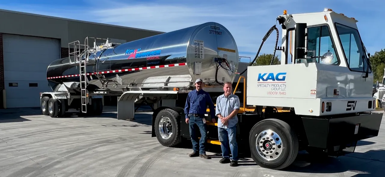 Two KAG Specialty Products Group employees standing beside a Kenan Advantage Group tanker trailer and a yard spotter truck