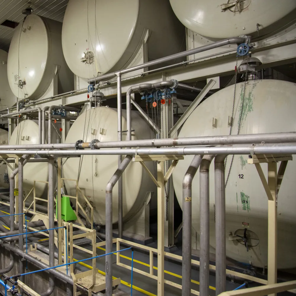 Indoor bulk storage facility with large horizontal storage tanks, piping infrastructure, and processing equipment used for industrial liquid storage and handling.