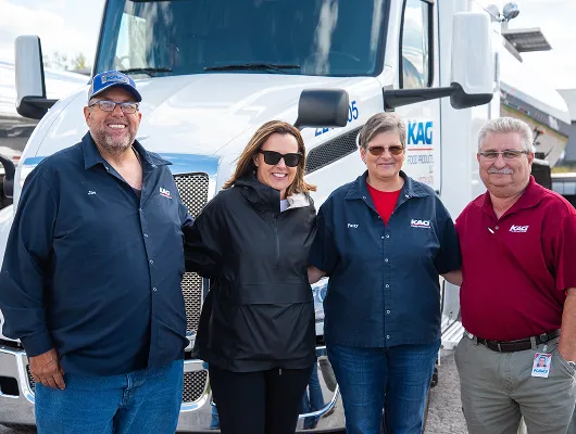 Four KAG employees smiling together in front of a KAG Food Products semi-truck