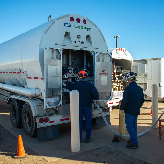 Two workers in hard hats and safety gear servicing the rear of a Clean Energy cryogenic tanker trailer outdoors