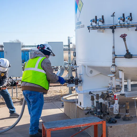 Two workers in safety gear and helmets operating valves on a hydrogen refrigerated liquid storage tank