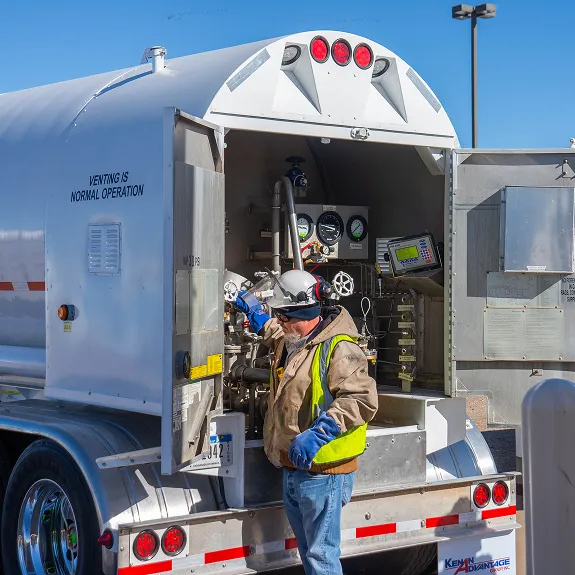 Technician in a high-visibility vest and hard hat inspecting the rear compartment of a cryogenic tanker trailer