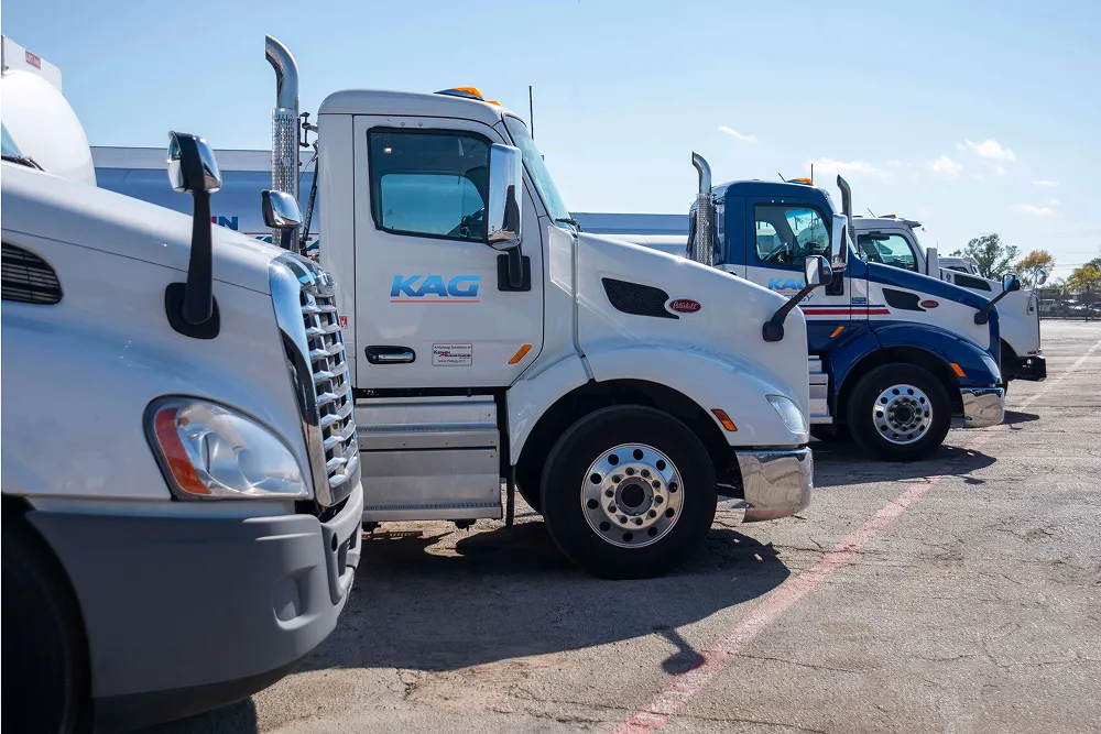Row of white and blue KAG truck cabs parked in a lot under a clear sky
