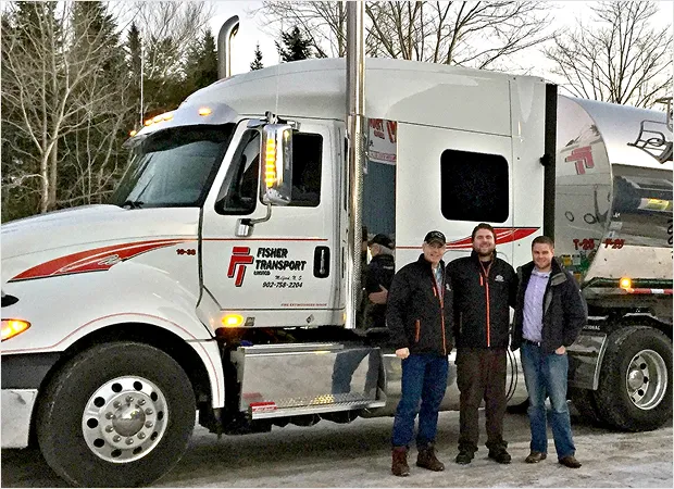 Three employees posing in front of a Fisher Transport tanker truck in a winter setting